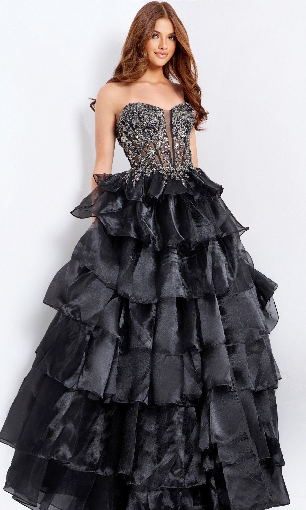 A woman in the Jovani 50259 long prom dress stands against a plain light background, showcasing its strapless black design with an embroidered corset bodice and a tiered, ruffled skirt.